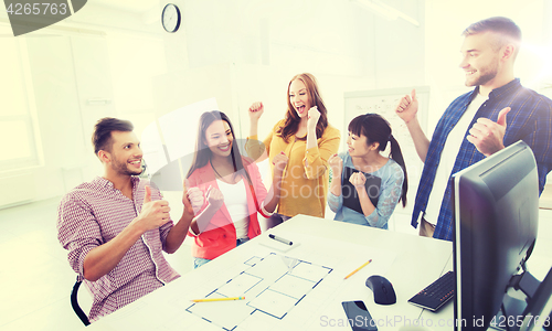 Image of happy creative team celebrating success at office