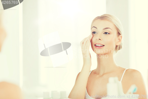 Image of happy woman applying cream to face at bathroom