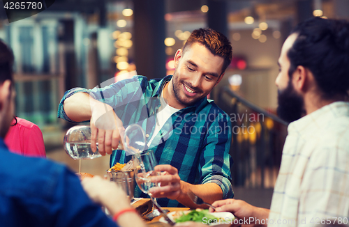 Image of happy man with friends pouring water at restaurant