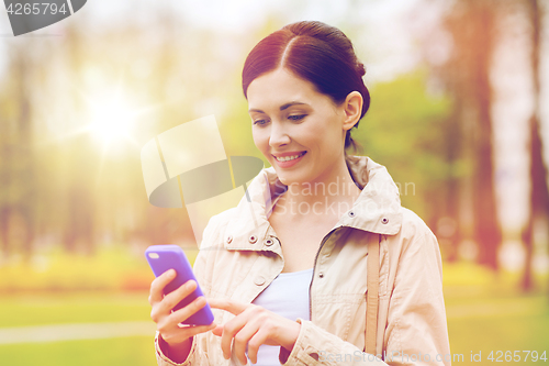 Image of smiling woman calling on smartphone in park