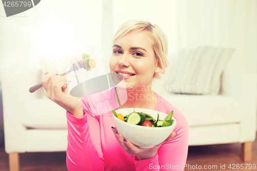 Image of smiling young woman eating salad at home