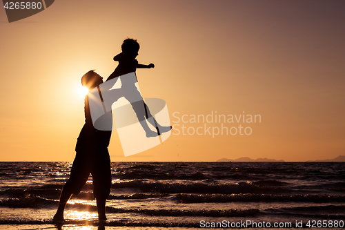 Image of Father and son playing on the beach at the sunset time.