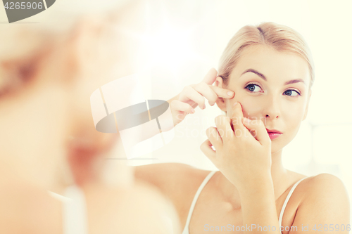 Image of woman squeezing pimple at bathroom mirror