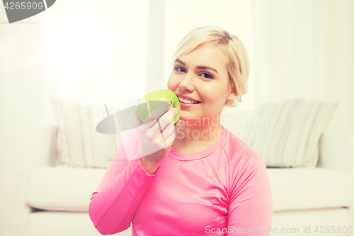 Image of happy woman eating apple at home