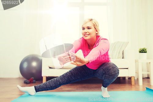 Image of happy woman stretching leg on mat at home