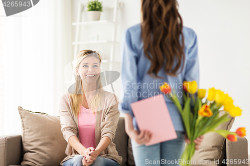 Image of happy girl giving flowers to mother at home