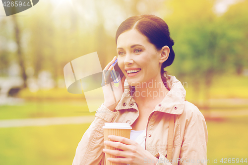 Image of smiling woman with smartphone and coffee in park