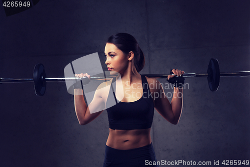 Image of young woman flexing muscles with barbell in gym