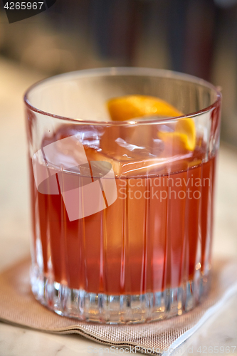 Image of close up of glass with orange cocktail at bar