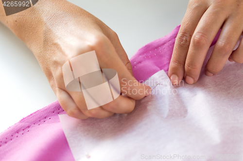 Image of woman with pins stitching paper pattern to fabric