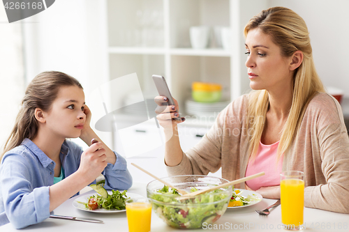 Image of sad girl looking at her mother with smartphone