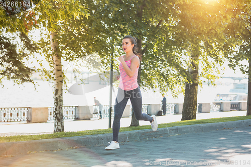 Image of Pretty sporty woman jogging at park in sunrise light