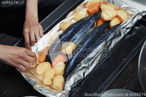 Image of Woman putting fish and vegetables to the baking sheet