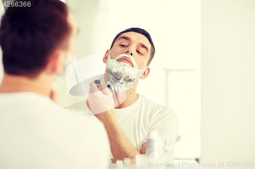 Image of man shaving beard with razor blade at bathroom