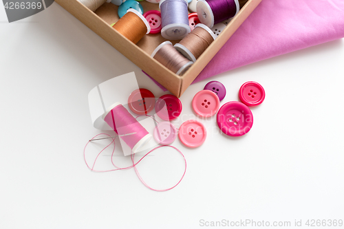 Image of box with thread spools and sewing buttons on table