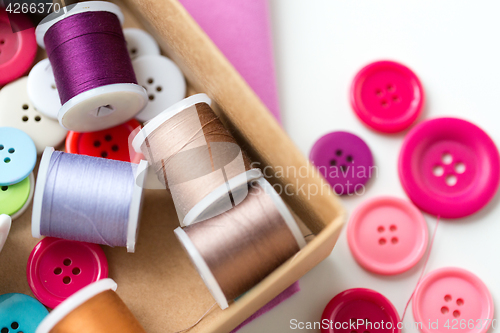 Image of box with thread spools and sewing buttons on table