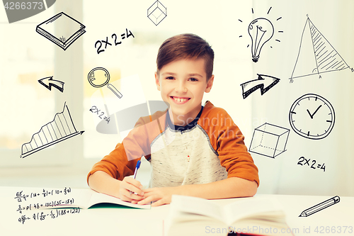 Image of smiling student boy writing to notebook at home