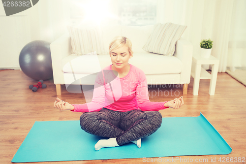 Image of happy woman stretching leg on mat at home