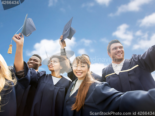 Image of happy bachelors waving mortar boards over sky