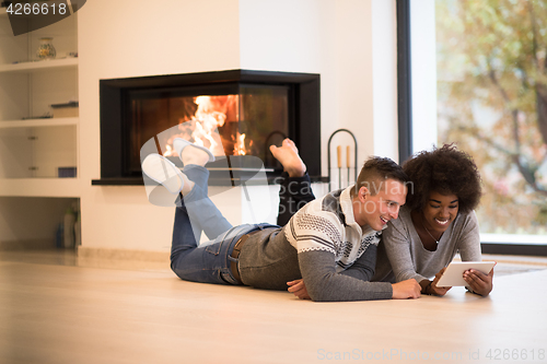 Image of multiethnic couple using tablet computer on the floor