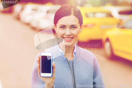 Image of smiling woman showing smartphone over taxi in city