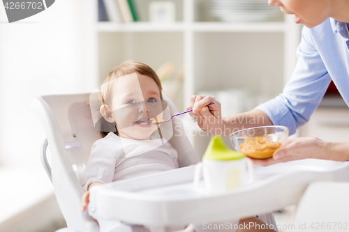 Image of happy mother feeding baby with puree at home