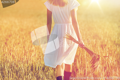 Image of young woman with cereal spikelets walking on field