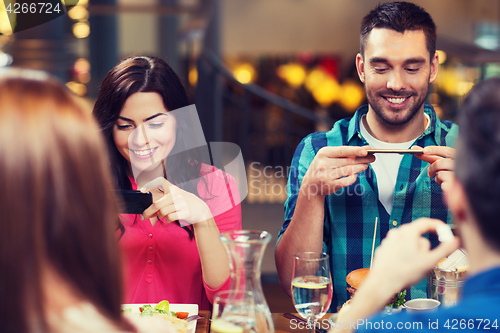 Image of happy friends taking picture of food at restaurant