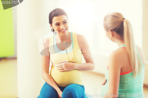 Image of two happy pregnant women sitting on balls in gym
