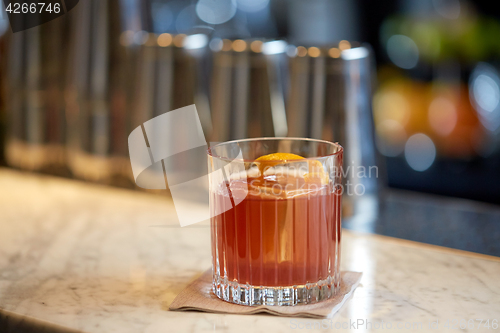 Image of glass of cocktail with orange peel at bar