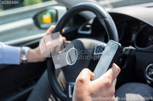 Image of Businessman texting on his mobile phone while driving.