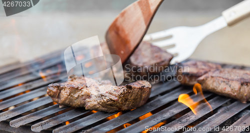 Image of Chef grilling beef steaks on open flame BBQ.