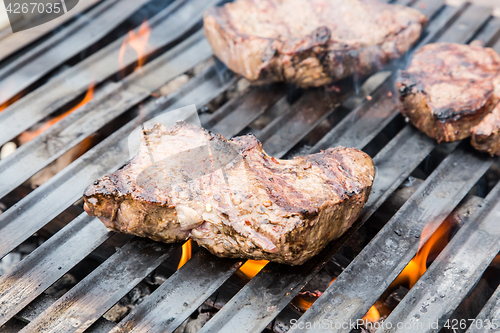 Image of Beef steaks on grill with flames.