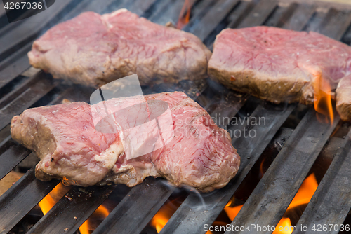 Image of Raw beef steaks on grill with flames.