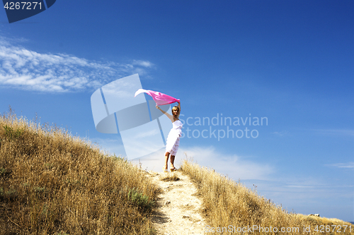 Image of portrait of beautiful blond woman in white dress standing on wind with scarf near sea