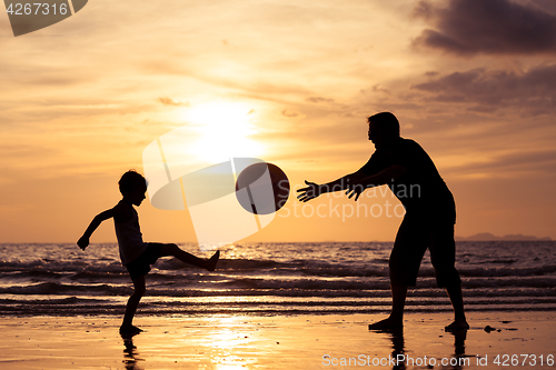 Image of Father and son playing on the beach at the sunset time.