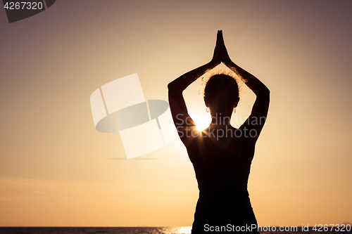 Image of woman open arms under the sunset at sea.