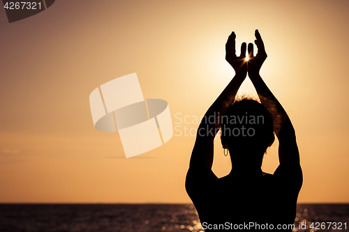 Image of woman open arms under the sunset at sea.