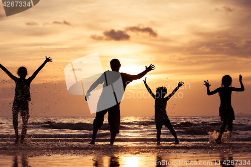 Image of Father and children playing on the beach at the sunset time.