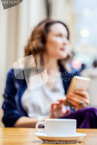 Image of cup of tea on the table and a woman with a smartphone in the blu