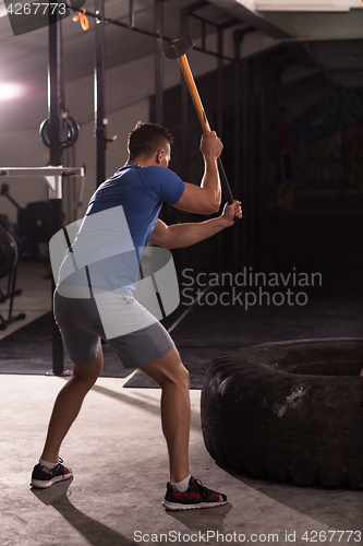 Image of man workout with hammer and tractor tire