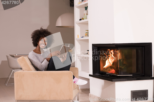 Image of black woman reading book  in front of fireplace