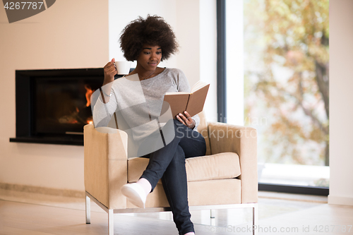 Image of black woman reading book  in front of fireplace