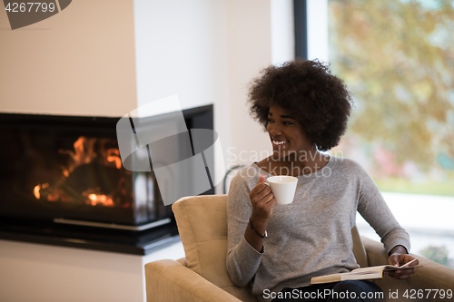 Image of black woman reading book  in front of fireplace