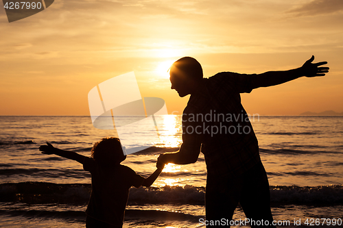 Image of Father and son playing on the beach at the sunset time.