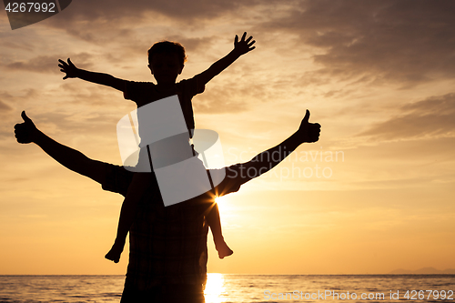 Image of Father and son playing on the beach at the sunset time.