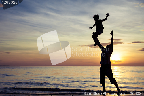 Image of Father and son playing on the beach at the sunset time.