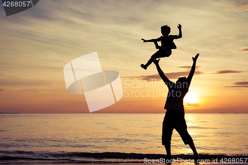 Image of Father and son playing on the beach at the sunset time.