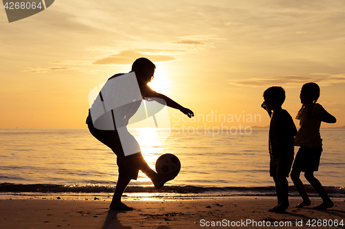 Image of Father and children playing on the beach at the sunset time.