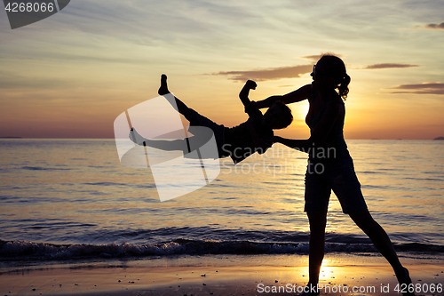 Image of Mother and son playing on the beach at the sunset time.